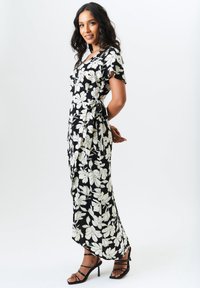 Floral wrap dress in black and white, featuring short sleeves, a V-neck, and a side tie. Paired with black strappy heels.