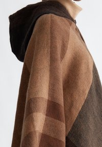 Hnědo-černý kostičkovaný svetr z vlněné směsi s kapucí, volného střihu a texturovaným povrchem, featuring výraznou kapuci a překrývajícími se vrstvami látky.