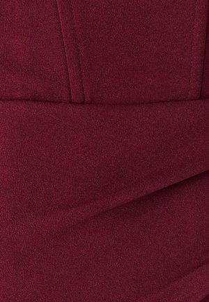 Burgundská texturovaná látka s hladkým povrchem, zdobená sklady a přiléhavým střihem, který zdůrazňuje čisté linie a jemný lesk.