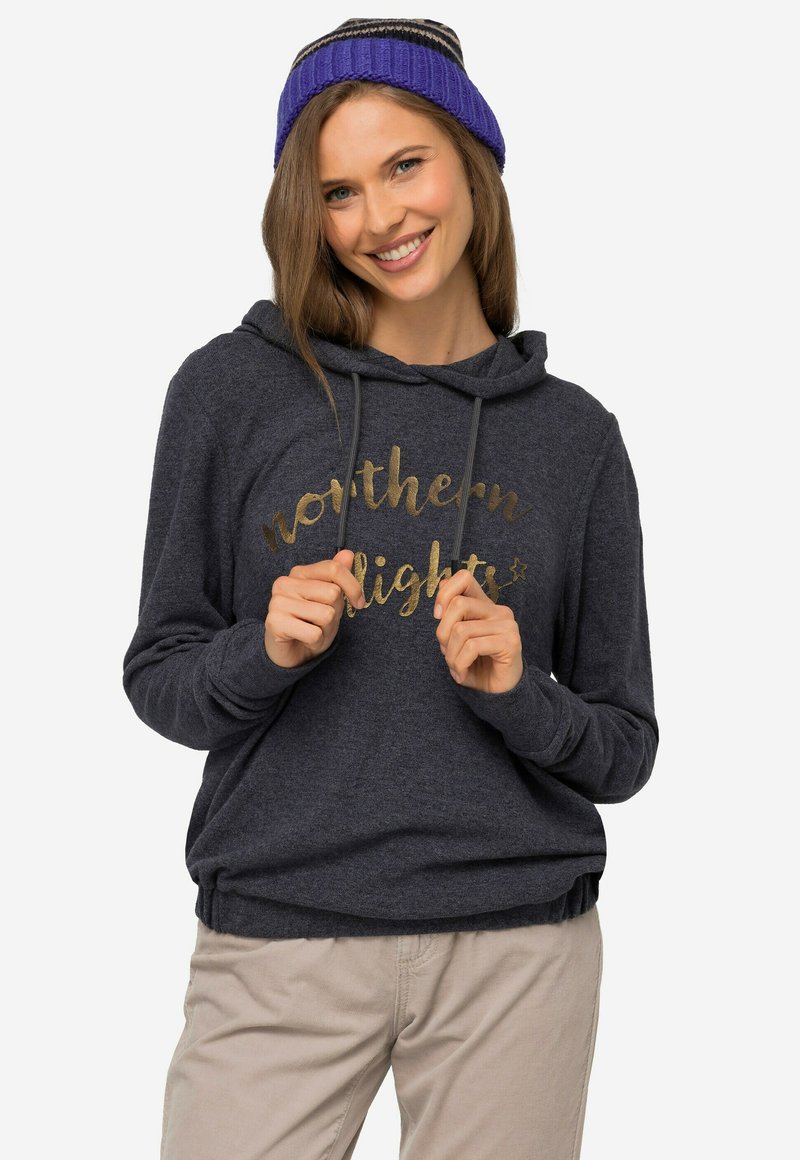 Mørkegrå hættetrøje med en guld, kursiv skrift, der står "northern lights." Modellen holder om manchetterne og bærer en lilla strikket beanie.