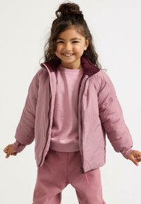Lyserød pufferjakke med maroon indvendig, lynlås og elastiske manchetter, båret over et matchende lyserødt outfit. Blød tekstur, afslappet design.