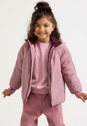 Lyserød pufferjakke med maroon indvendig, lynlås og elastiske manchetter, båret over et matchende lyserødt outfit. Blød tekstur, afslappet design.