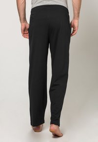 Schwarze, leichte Freizeithosen mit elastischem Bund, geradem Schnitt und ohne Muster. Die Ansicht zeigt die Rückseite und den Saum, mit sichtbaren baren Füßen.