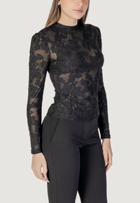 Blusa nera a maniche lunghe realizzata in tessuto trasparente con un motivo floreale ricamato. La silhouette è aderente in vita e lo scollo è alto.