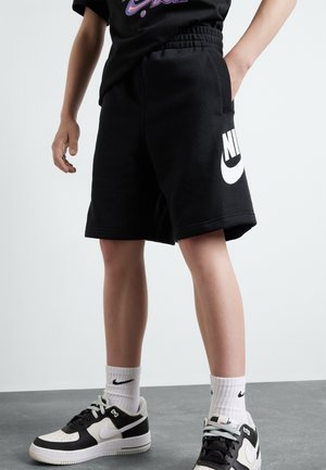 Shorts Nike noirs avec logo blanc, taille élastique, poches avant, associés à des baskets Nike noires et blanches et chaussettes blanches.
