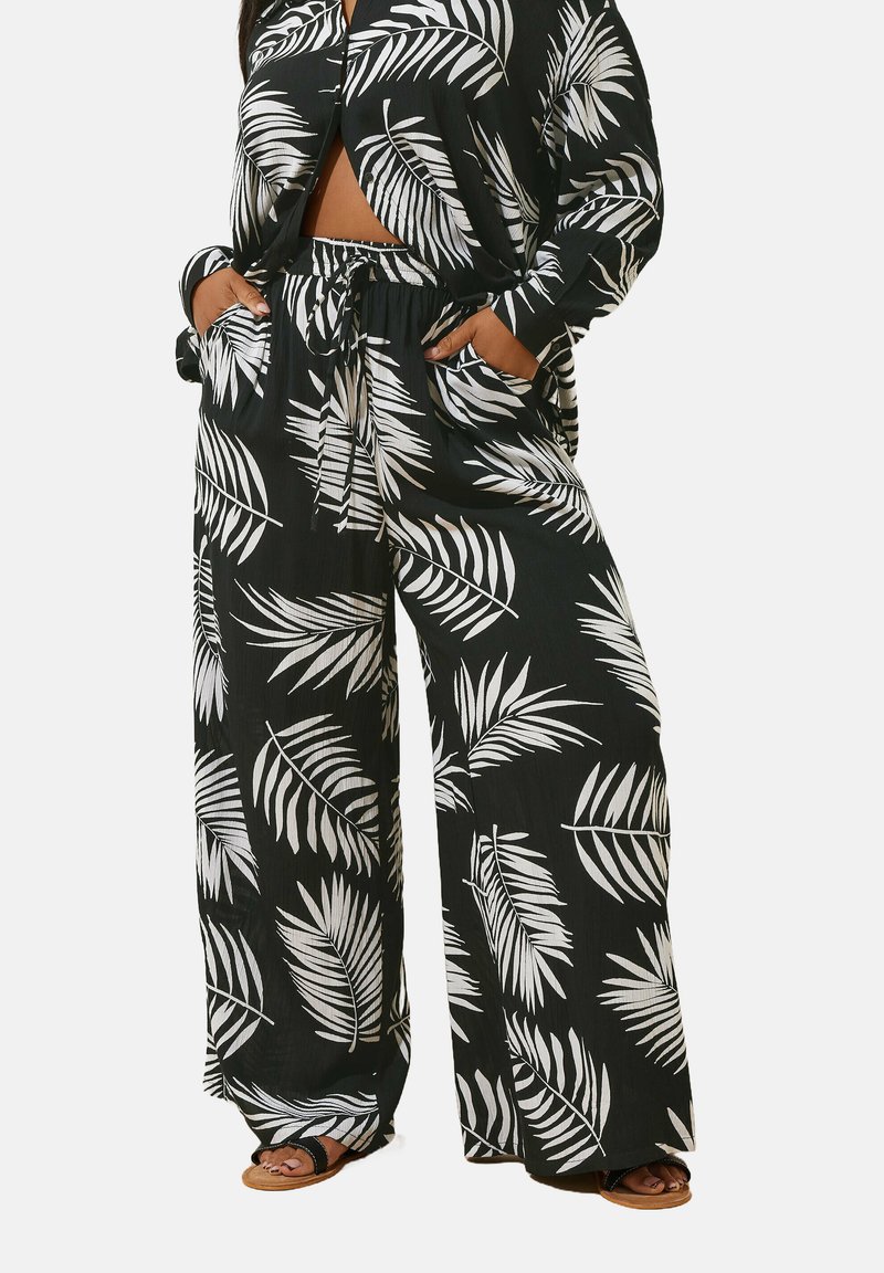 Svart outfit med vita lövmönster, bestående av lösa byxor med resårmidja och en matchande knäpptopp.