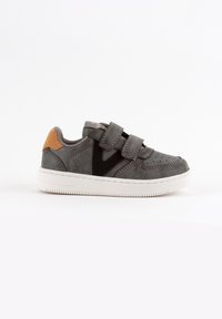 Zapatilla de ante gris con tiras de Velcro, un logo V negro y un acento naranja en el talón. Suela de goma blanca. Textura suave.