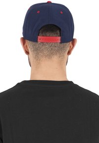 Állítható baseball sapka tengerészkék koronával, piros részletekkel és műanyag snapback záródással. Simaságot biztosító textilből készült.
