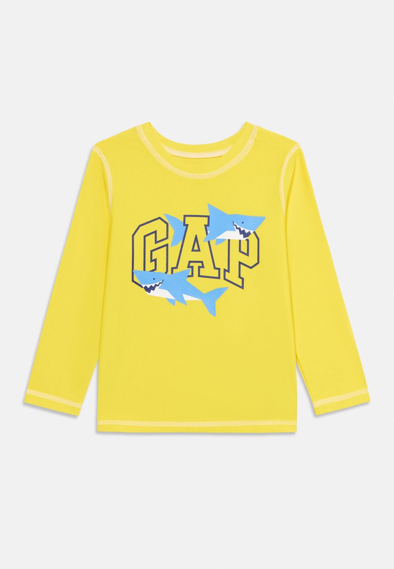 Chemise jaune à manches longues pour enfants avec le texte « GAP » et deux requins dessin animés bleus imprimés sur le devant.
