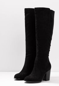 Czarne kozaki sięgające do kolan, wykonane z miękkiego zamszu. Posiadają solidny obcas, zaokrąglony nosek oraz gładki, bezszwowy design bez widocznych elementów metalowych.