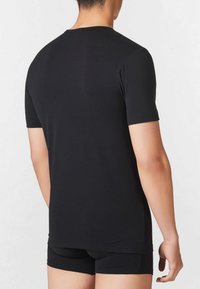 T-shirt nera a maniche corte realizzata in morbido cotone con scollatura rotonda, caratterizzata da un design aderente e una texture liscia, indossata con pantaloni corti neri.