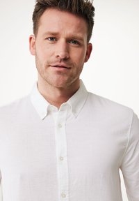 Camisa blanca de botones hecha de lino ligero, con un cuello clásico y una textura sutil, con una tapeta de botones y puños visibles.