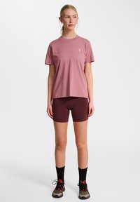 Lyserød kortærmet t-shirt med rund hals, parret med bordeaux atletikshorts. Sorte knæhøje strømper og multicolor sneakers fuldender looket.