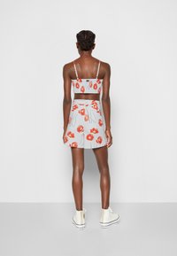 Top curto floral e saia combinando com flores vermelhas sobre um fundo cinza claro. A modelo usa tênis brancos. Vista traseira com alças finas.