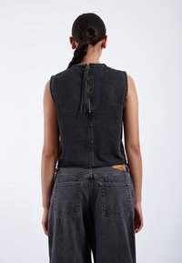 Sleeveless black denim jumpsuit with back zipper detail, featuring a relaxed fit, side pockets, and a woven tan label on the waistband.