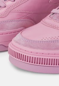 Pink sneakers featuring a combination of smooth leather and soft suede textures, with detailed stitching and a ridged rubber sole.