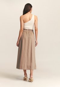 Ribbed white tank top dengan satu bahu, dipadukan dengan rok panjang beige yang mencapai pergelangan kaki dan memiliki pinggang elastis serta tekstur halus.