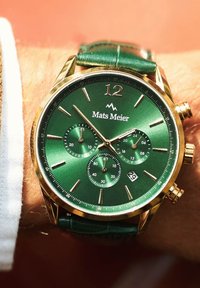 Grüne Chronographuhr mit goldenem Gehäuse, drei Hilfszifferblättern und grünem Lederarmband. Markierungen und Datumsanzeige sind sichtbar.