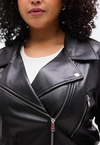 Μαύρο δερμάτινο μπουφάν από συνθετικό δέρμα με γιακά με εγκοπή, ασύμμετρο φερμουάρ και ασημένιες μεταλλικές λεπτομέρειες. Ομαλή υφή, με πολλαπλές τσέπες με φερμουάρ.