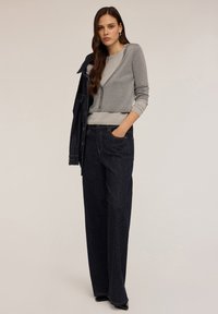 Grå cardigan över ljusgrå topp, tillsammans med mörkbå jeans med vita polka prickar. Modellen står med ena handen i fickan och bär klackar.