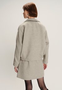 Blazer grigio chiaro con una vestibilità rilassata, spalle basse e cintura elastica, abbinato a una gonna grigio chiaro coordinata. Tessuto strutturato.