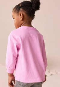 Lyserød langærmet skjorte lavet af blødt stof, med rund halsudskæring og ribbede manchetter, parret med grå jeans.