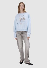 Jasnoniebieska, oversize bluza z nadrukiem, zestawiona z jasnoszarymi prostymi dżinsami. Całość dopełniają czarne baleriny z noskiem w szpic.