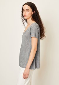 Pilkos spalvos trumpomis rankovėmis palaidinė su V formos iškirpte, pagaminta iš tekstūrizuotos, lengvos medžiagos. Laidūs siluetas su išlenktu hemu, derinama su baltais džinsais.