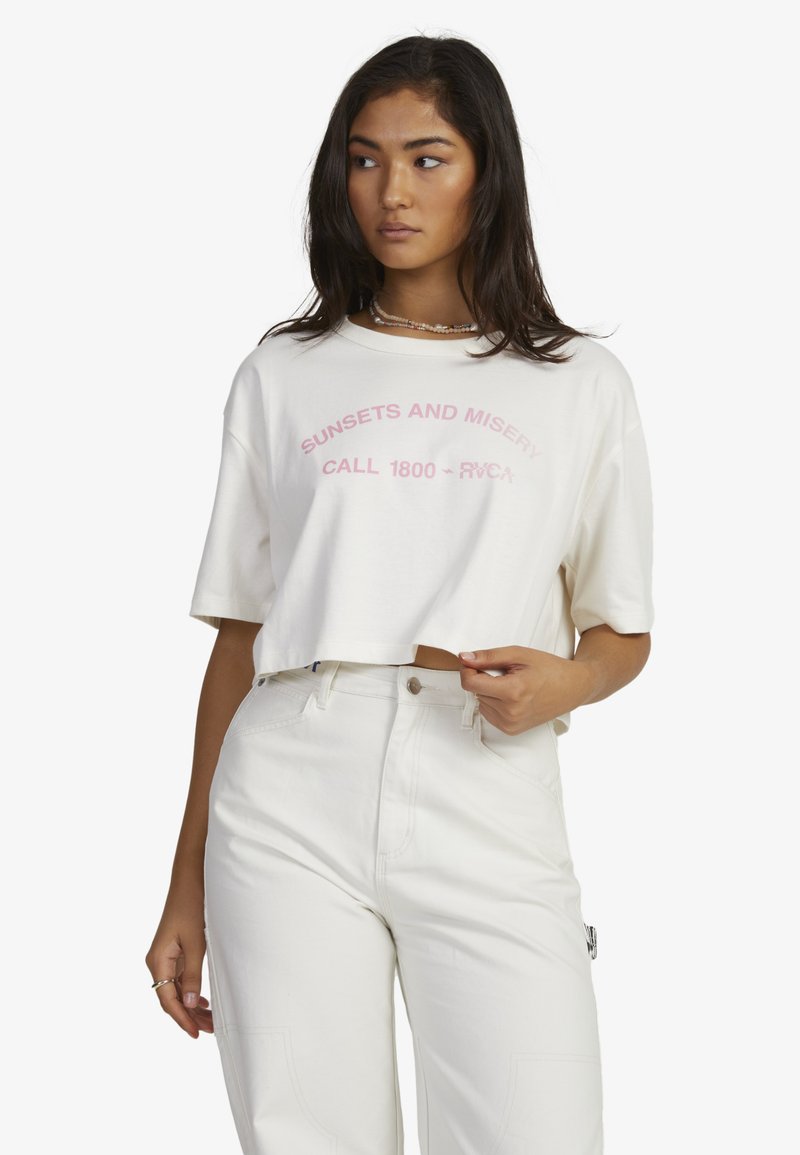 White cropped t-shirt with pink printed text, "SUNSETS AND MISERY CALL 1800 - RVCA." Short sleeves, soft texture, relaxed fit.