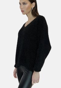 Maglione nero e fluffy con scollatura a V e spalle scese; indossato con leggings neri lucidi; tessuto morbido e vestibilità rilassata.