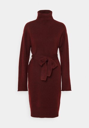 Robe en maille rouge foncé à manches longues, col montant et ceinture en tissu nouée à la taille, longueur genou sur fond blanc.
