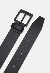 Ceinture en cuir noir avec une boucle en métal noir mat de forme rectangulaire. Comprend cinq trous pour l'ajustement et une extrémité effilée pour un passage facile.