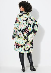 Un long hoodie noir avec des textes et des motifs dans un style graffiti vibrants aux couleurs néon. Tissu lisse ; coupe décontractée avec une capuche. Leggings noirs et bottes cloutées.