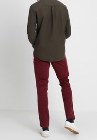 Langsleeve, donkergroene blouse met een afgeronde zoom en een rugplooitje, gecombineerd met slim-fit bordeauxrode broek en witte sneakers.