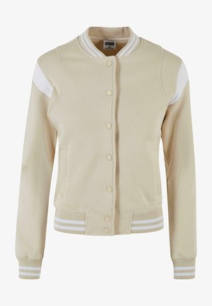 Veste varsity beige avec des accents blancs sur les épaules, col et poignets côtelés. Elle dispose de boutons-pression et de deux poches avant. Matière douce.