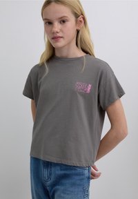 Gray cotton t-shirt with short sleeves, featuring pink graphic text on the chest. Styled with loose blue jeans.