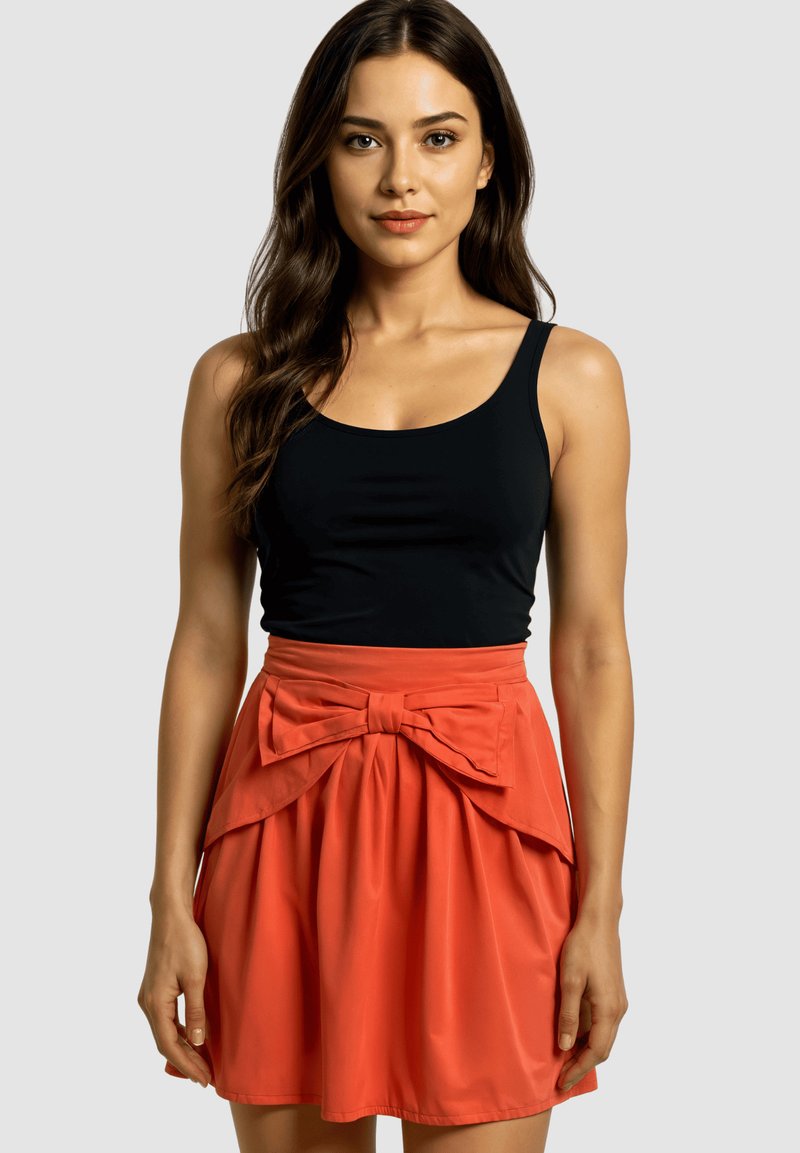 Top negro sin mangas combinado con una falda naranja que presenta un gran lazo en la cintura. La falda tiene una textura suave y fruncida.