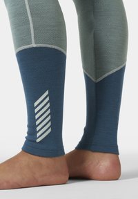 Leggings con una parte superior texturizada en verde y una sección inferior en azul con un diseño de rayas blancas, hechos de un material elástico.