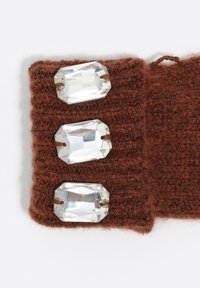 Brązowy dziergany tekstyl z trzema wyraźnymi, prostokątnymi kamieniami szlachetnymi przymocowanymi, prezentujący teksturowaną powierzchnię i dekoracyjne detale.