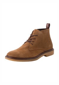 Bottes chukka en daim marron avec un bout rond, un système de laçage à l'avant et une semelle en caoutchouc texturée. Présentent un talon brun contrastant et une languette.