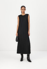 Rochie maxi plisată, de culoare neagră, cu decolteu rotund, design fără mâneci și textură netedă. Purtați cu cizme negre până la glezne și o geantă mică.