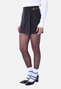 Gonna nera con cintura, design plissettato, abbinata a collant neri trasparenti e dècolletè in vernice. Calzini bianchi alla caviglia aggiungono contrasto.