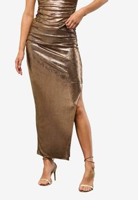 Metaalachtige bronzen jurk met geplooide buste, tot de knie hoge split en vloeiende ontwerp. Gecombineerd met naakte, strappy hoge hakken.