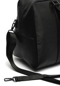 Schwarze Ledertasche mit texturierter Oberfläche, ausgestattet mit einem abnehmbaren Nylonriemen und Metallbeschlägen. Reißverschluss oben und seitliche Tasche sichtbar.