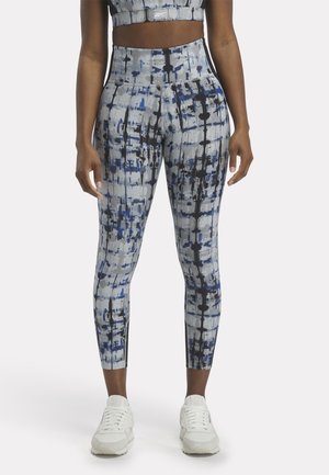 Leggings in un motivo astratto blu e grigio, design a vita alta, realizzati in materiale elasticizzato, abbinati a scarpe sportive bianche.