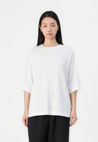 Witte katoenen t-shirt met korte, brede mouwen en een ronde halslijn. Eenvoudige, relaxte pasvorm, gecombineerd met zwarte, losse broek.