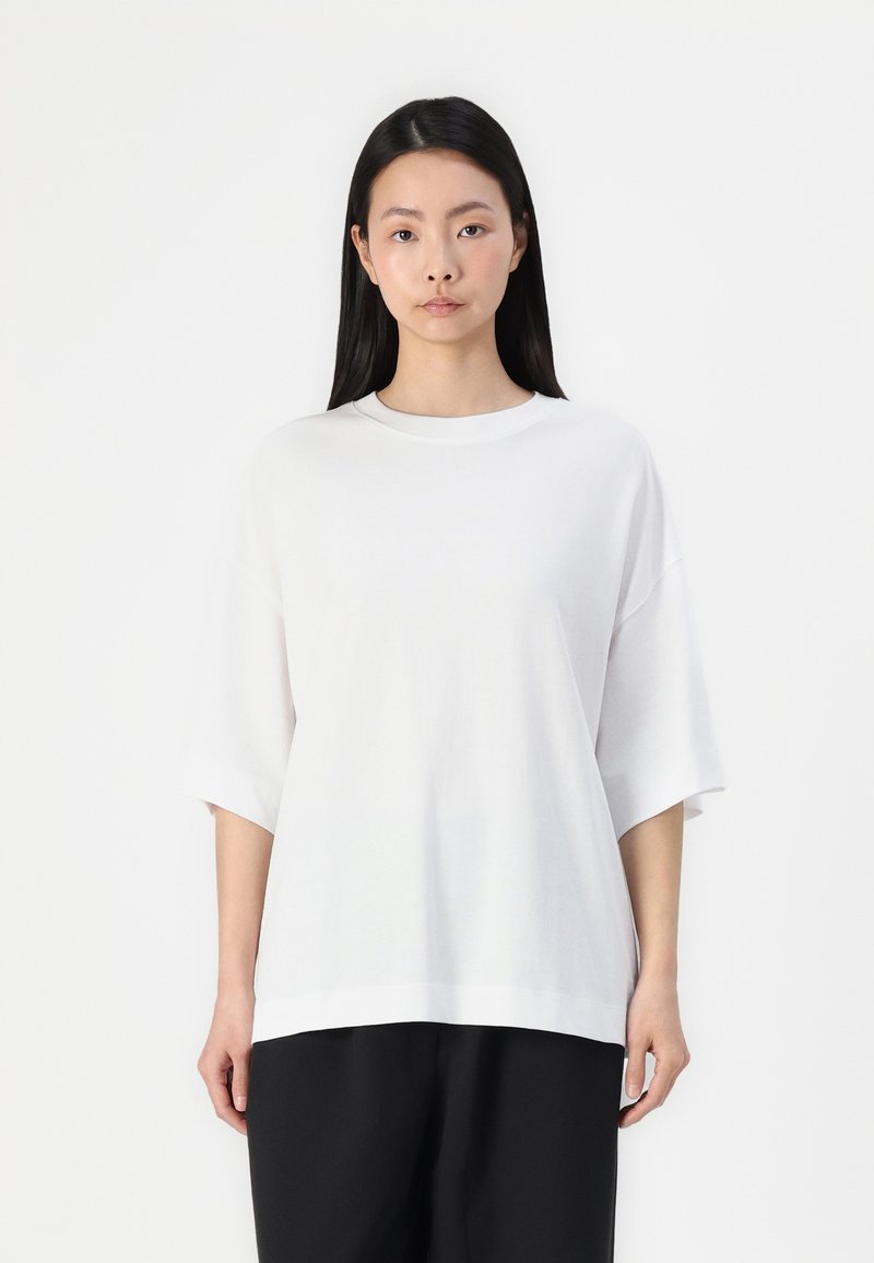 Witte katoenen t-shirt met korte, brede mouwen en een ronde halslijn. Eenvoudige, relaxte pasvorm, gecombineerd met zwarte, losse broek.
