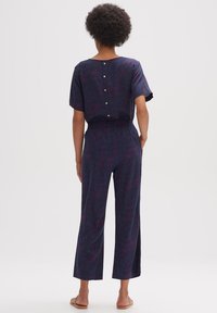 Marineblauwe jumpsuit met korte mouwen, elastische taille en knoopsluiting aan de achterkant; heeft een gemarmerd patroon in roze en paarse tinten.