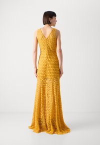 Gul lacekjole med en tettsittende silhuett, V-ryggdesign, blomster mønster, og en utsvingt hem som når gulvet.