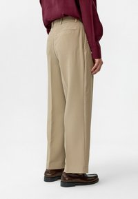 Licht beige gestreepte broek met een relaxte pasvorm, achterzakken en een gladde textuur, gecombineerd met bruine nette schoenen.